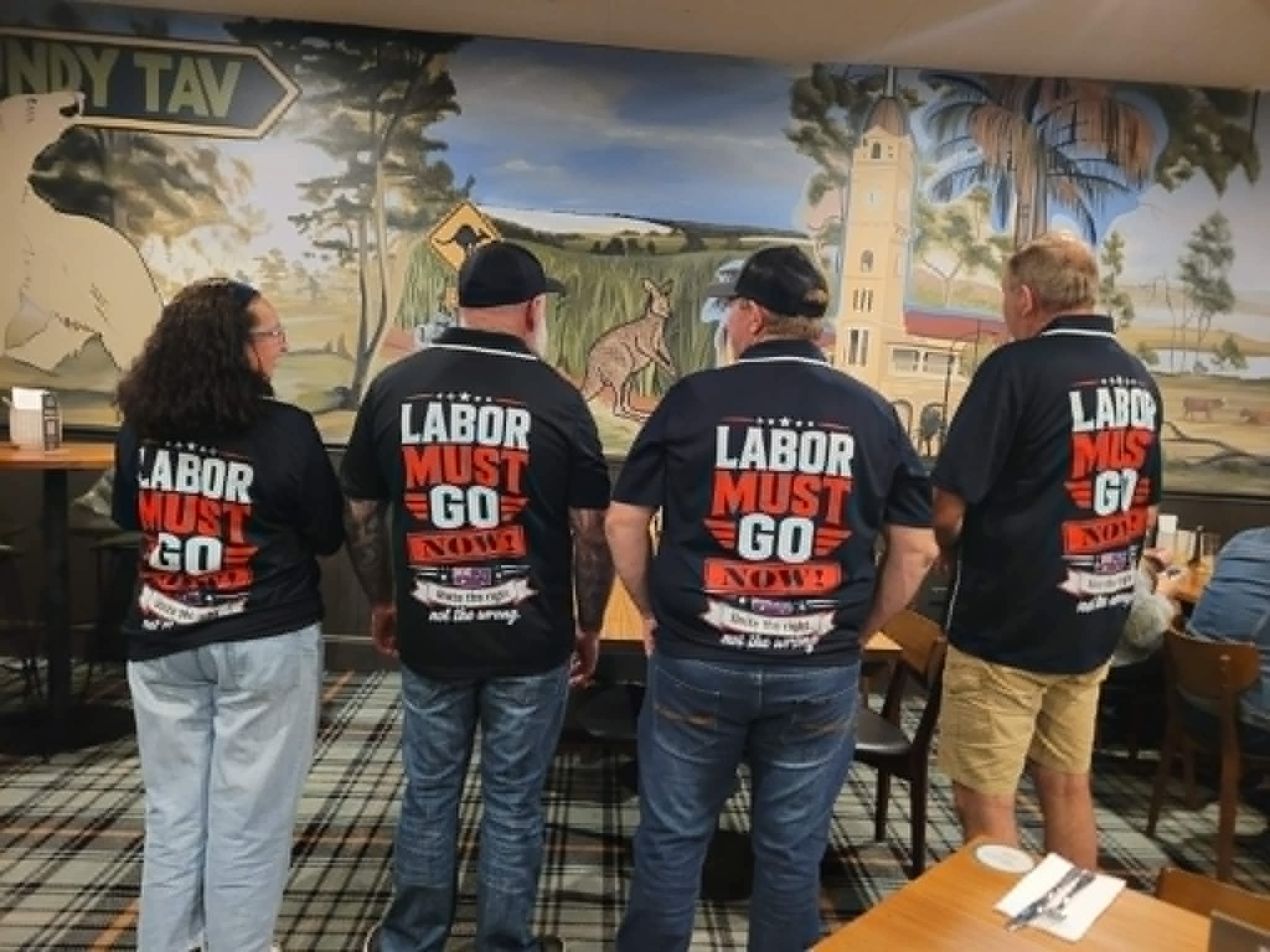 Four supporters wearing Labor Must Go Now collared shirts at a community gathering